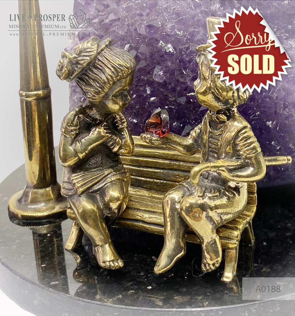 Bronze figures of cupid and sweethearts on a bench with a garnet heart on geodes amethyst agate background
